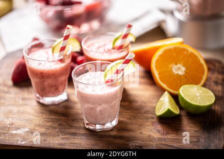 Vari frullati di frutta in tazze di vetro con cannucce di carta e spicchi di calce e più citrus sul lato. Foto Stock