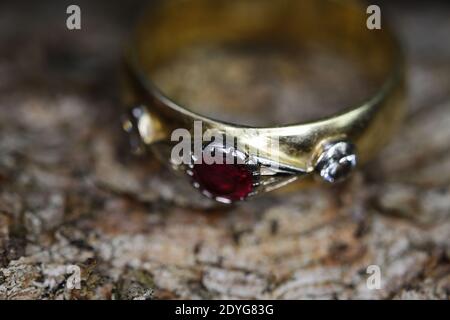 Primo piano dell'isolato anello d'oro vintage con diamante e gemma rosso rubino sullo sfondo naturale della corteccia del tronco dell'albero Foto Stock