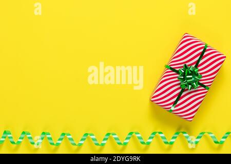 Confezione regalo a righe con arco verde su sfondo di carta giallo. Cartolina con nastro a serpentina, modello minimo. Festivo mockup con poliziotto Foto Stock