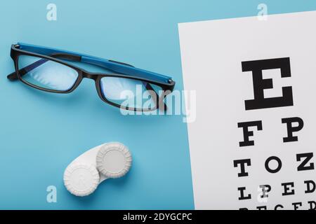 Occhiali con lenti a contatto, gocce e una tabella di prova dell'occhio di Optometrist su uno sfondo blu. La vista dall'alto. Spazio libero Foto Stock