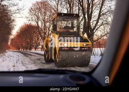 Rullo in asfalto durante le riparazioni su strada in inverno, vista dalla vettura. Foto Stock