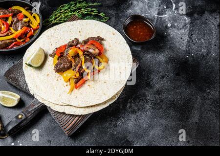 Fajitas messicane con peperoni e cipolle colorate, servite con tortillas e salsa. Sfondo nero. Vista dall'alto. Spazio di copia Foto Stock