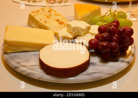 Una selezione di deliziosi formaggi e uve su marmo cheeseboard Foto Stock