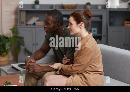 Giovane coppia multietnica seduta su divano su consultazione in ufficio Foto Stock