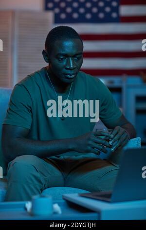 Giovane africano che beve alcolici e guarda qualcosa sul computer portatile mentre si è seduti sul divano Foto Stock