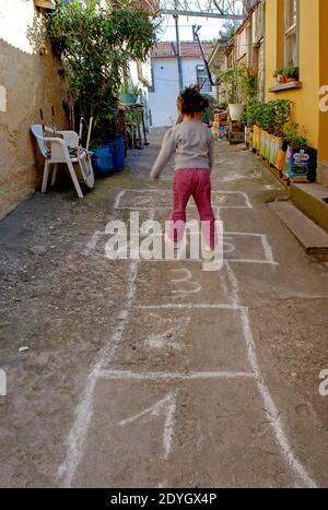 Giochi per bambini di strada`s in classici. Bambina che gioca hopscotch disegnato con gesso sul pavimento Foto Stock