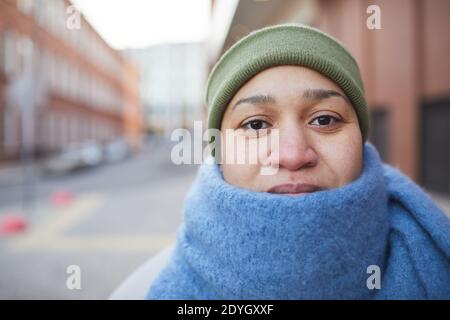 Ritratto di giovane donna in caldo sciarpa e cappello guardando a macchina fotografica mentre camminando sulla strada in tempo freddo Foto Stock