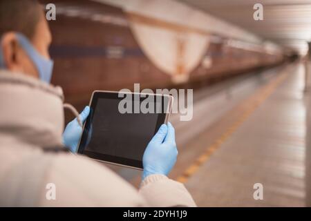 Vista posteriore della donna in maschera protettiva e in protezione guanti che tengono un tablet digitale e che leggono online Foto Stock