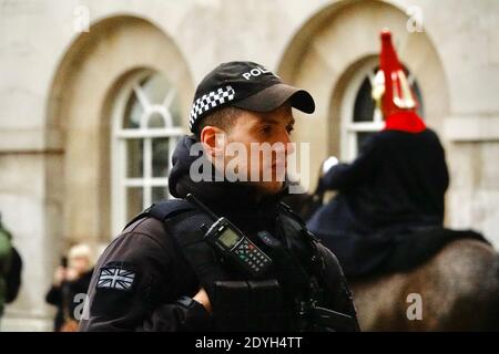 Ufficiale di polizia armato maschile che indossa un cappello da baseball in piedi durante il cambio della guardia alla Horse Guard’s Parade, Londra Foto Stock