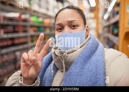 Ritratto di giovane donna in maschera protettiva facendo ritratto selfie sul suo telefono nel supermercato Foto Stock