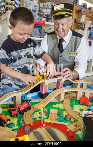 Alabama Calera Heart of Dixie Railroad Museum, ragazzo bambino visitatore anziano uomo maschio direttore uniforme volontario, aiutando a giocare binari giocattolo ferrovia, Foto Stock