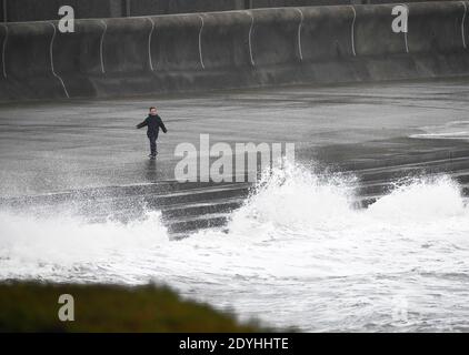 Porthcawl, Galles, 26 dicembre 2020 UN bambino cammina lungo il lungomare mentre Storm Bella colpisce Porthcawl durante l'alta marea di Porthcawl, la sera del Santo Stefano, mentre pioggia e forti venti colpiscono parti del Regno Unito. Foto Stock