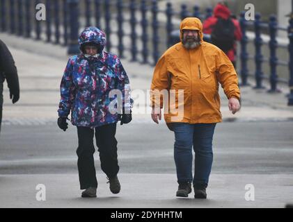 Porthcawl, Galles, 26 dicembre 2020 le persone che indossano abiti invernali come impermeabili lottano per camminare nel vento mentre Storm Bella colpisce Porthcawl in alta marea a Porthcawl, la sera di Santo Stefano, mentre pioggia e forti venti colpiscono parti del Regno Unito. Foto Stock