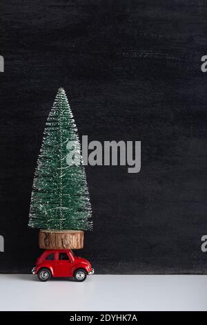 L'automobile giocattolo trasporta l'albero di Natale in miniatura. Consegna di alberi di Natale. Telaio verticale Foto Stock