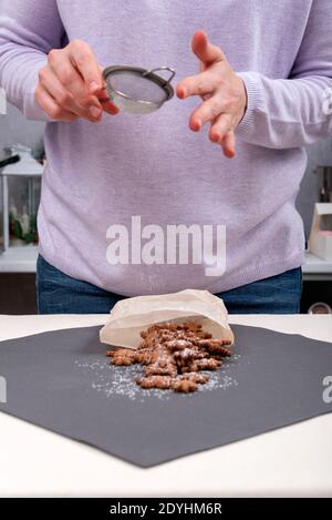 Lo chef della pasticceria spolvera i biscotti con zucchero a velo. Telaio verticale. Foto Stock