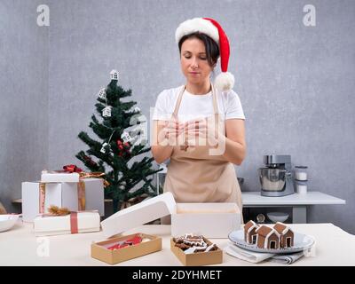 Lo chef di pasticceria della donna sta imballando i regali con i dolci di Natale. Biscotti al pan di zenzero. Foto Stock