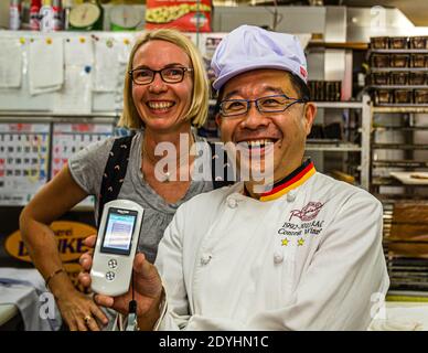 Panificio tedesco Danke a Izunokuni, Giappone. Daiichi Sugiyama indossa la giacca di un panettiere con le strisce nero-rosso-oro della bandiera tedesca e utilizza un traduttore di lingua mobile con virtuosità Foto Stock