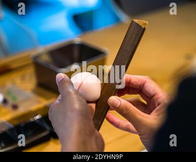 Due mani modellano un impasto wagashi rotondo e ceroso con uno strumento di legno stretto – laboratorio di pasticceria a Izu, Giappone. Foto Stock