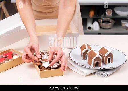 Le mani femminili mettono i biscotti del pan di zenzero nelle scatole di regalo. Casa di pan di zenzero e biscotti verniciati smaltati. Foto Stock