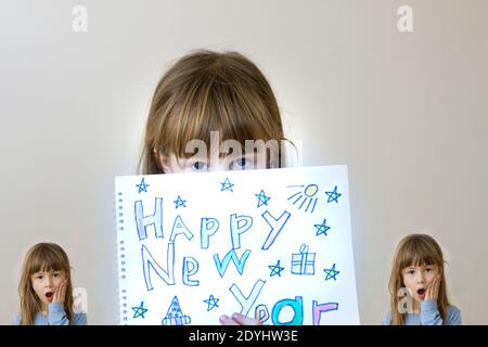 Collage di tre ragazze del bambino con l'espressione divertente del volto che tiene il disegno colorato felice anno nuovo su sfondo chiaro. Foto Stock