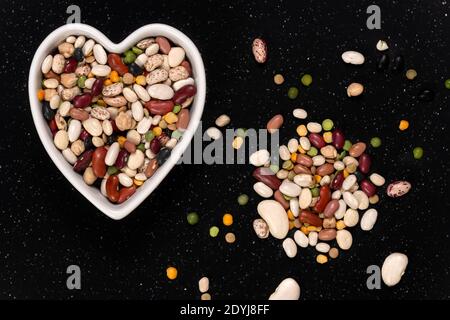 Piselli e fagioli misti per la zuppa in un fondo a forma di cuore e la consistenza della ciotola. Vista dall'alto. Foto Stock