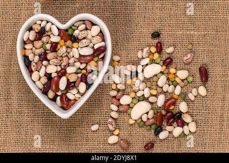 Piselli e fagioli misti per la zuppa in un fondo di ciotola a forma di cuore e consistenza. Vista dall'alto. Foto Stock