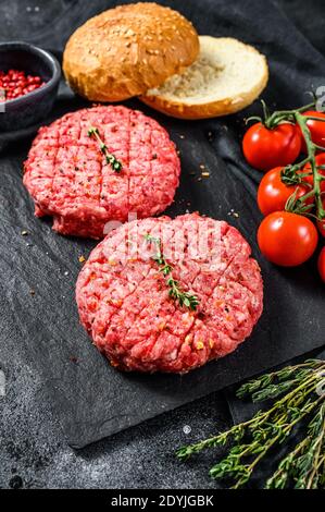 Ingredienti per la cottura degli hamburger. Polpettine di manzo tritato, focaccine, pomodori, erbe e spezie. Sfondo nero. Vista dall'alto Foto Stock