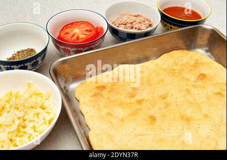 Pizza rettangolare fatta in casa - pasta per pizza e ingredienti: Formaggio, origano, pomodori a fette, tonno e salsa di pomodoro. Foto Stock