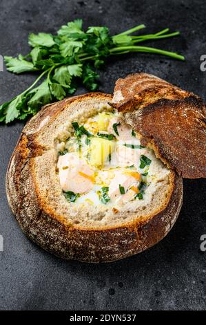 Zuppa finlandese di pesce cremoso con salmone, trota, patate servite nel pane. Sfondo nero, vista dall'alto. Foto Stock