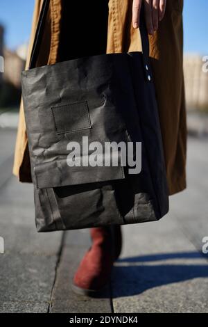 Sacchetto di carta riciclata nelle mani di una ragazza che indossa cappotto arancione e scarpe rosse. Zero sacchetti di rifiuti o concetto di moda. Foto Stock