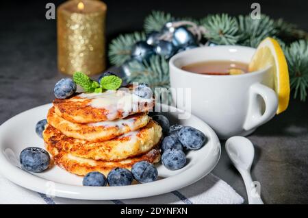 Frittelle calde fritte fatte in casa di formaggio cottage con latte condensato sul tavolo, decorato per Natale. Foto Stock