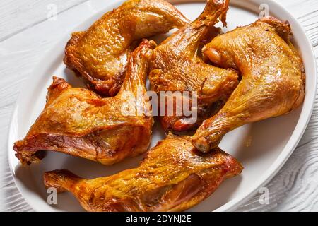 primo piano di cosce di pollo arrostite servite su un piatto bianco su un tavolo di legno, vista orizzontale dall'alto Foto Stock