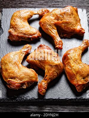 cosce di pollo arrosto croccanti servite su un vassoio di ardesia nera su un tavolo di legno scuro, vista orizzontale dall'alto Foto Stock