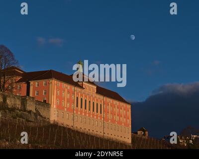 Edificio storico con facciata dipinta di rosa nella splendida luce notturna sopra i pendii dei vigneti con cielo blu chiaro e luna visibile nella città di Meersburg. Foto Stock