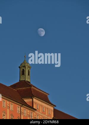 Vecchio edificio con facciata decorata di colore rosa e torre campanaria sul tetto in bella sera sole con luna visibile nel cielo blu e chiaro. Foto Stock