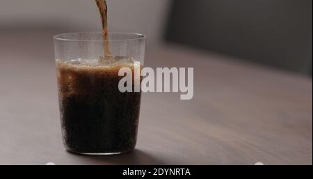 versare la cola nel bicchiere con ghiaccio sul tavolo in noce con spazio per la copia, foto ampia Foto Stock