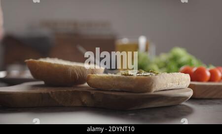 Uomo stendendo pesto su piccola ciabatta per panino su bancone cucina, foto ampia Foto Stock