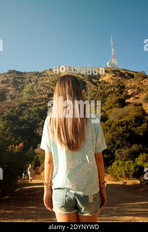 Vista posteriore della ragazza che guarda l'insegna di Hollywood, Los Angeles, California, Stati Uniti. Foto da viaggio in stile Instagram. Ago 2019 Foto Stock