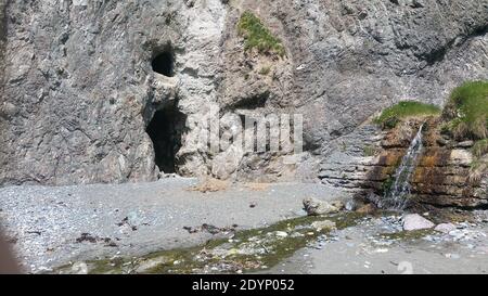 Ingresso alle grotte su una spiaggia appartata con il ruscello che scende dal pendio. Foto Stock