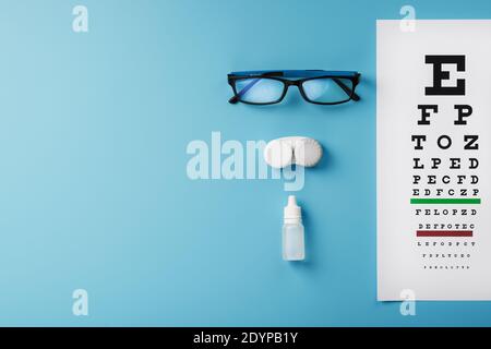 Occhiali con lenti a contatto, gocce e una tabella di prova dell'occhio di Optometrist su uno sfondo blu. La vista dall'alto. Spazio libero Foto Stock