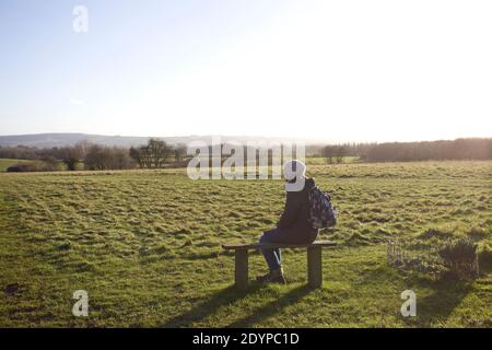 Giovane donna sedette sulla panchina rilassandosi al sole d'inverno, Oxfordshire England Foto Stock