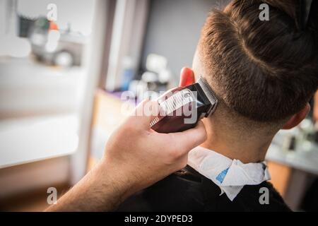 Primo piano di una mano del Barbiere che sta tagliando i capelli a. un cliente nella sua casa barbiere Foto Stock