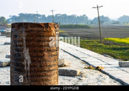 Vecchio tamburo di ferro arrugginito su un sito di costruzione accanto al primo piano campo agricolo Foto Stock