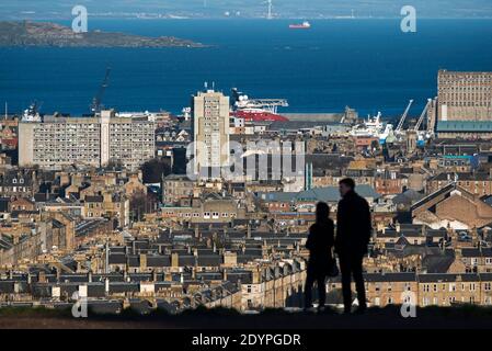 La silhouette di una coppia che si trova sulla collina di Calton guardando verso nord verso Leith e il Firth of Forth a Edimburgo, Scozia, Regno Unito. Foto Stock