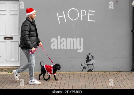 Camminando il cane in un vestito di Babbo Natale il Natale Giorno con un messaggio di speranza su un muro Foto Stock