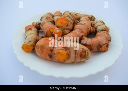 Primo piano di rizoma curcuma colorato arancione (curcuma longa) su piastra bianca. Curcuma crudo di colore arancio proveniente dall'India Asia. Pezzi heap. Utilizzato per coo Foto Stock