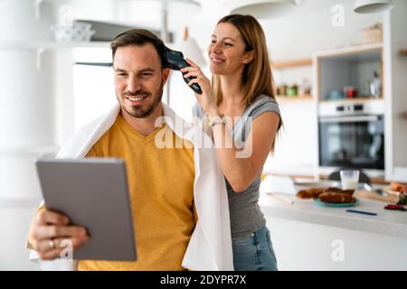 Coppia che ha i capelli tagliati a casa durante la quarantena coronavirus pandemico, online parrucchiere su tablet Foto Stock