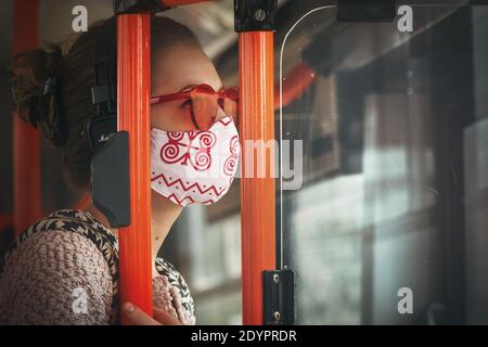 Donna che indossa una maschera in tessuto fatta in casa a bordo di un autobus pubblico. Si consiglia di indossare maschere facciali per rallentare la diffusione del virus corona. Foto Stock