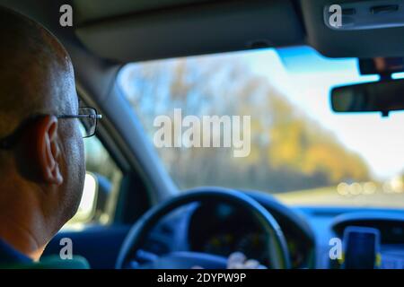 Uomo anziano con occhiali che guidano un'automobile mentre guidano la vista posteriore Russia, regione di Kursk, Zheleznogorsk, ottobre 2016. Messa a fuoco selettiva sul cristallo del conducente Foto Stock