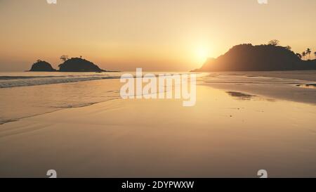 Silhouette di isole paradisiache di montagna al tramonto. Il sole aereo riflette la luce sul mare. Le onde della baia del mare si infrangono alla spiaggia di sabbia. Serata di sole alle Filippine, Asia. Nessuno paesaggio naturale Foto Stock